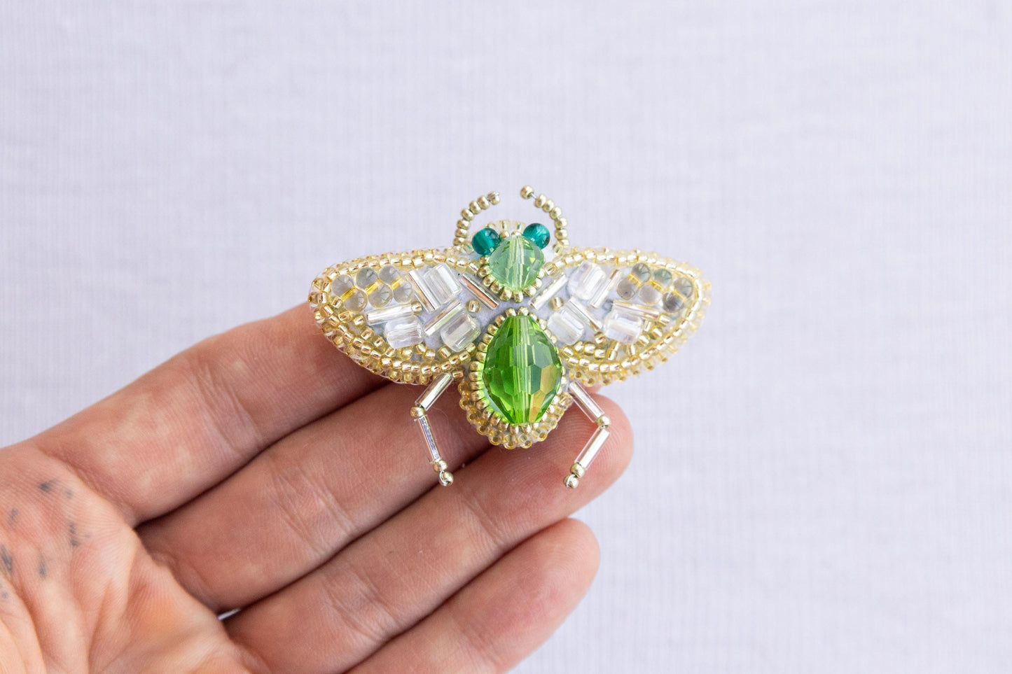 a hand holding a green and white insect brooch
