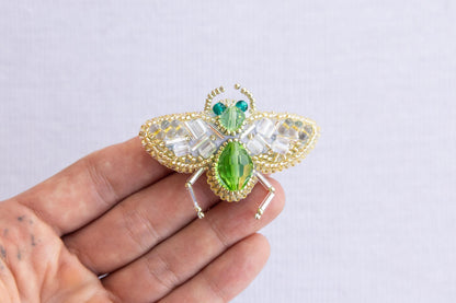 a hand holding a green and white insect brooch