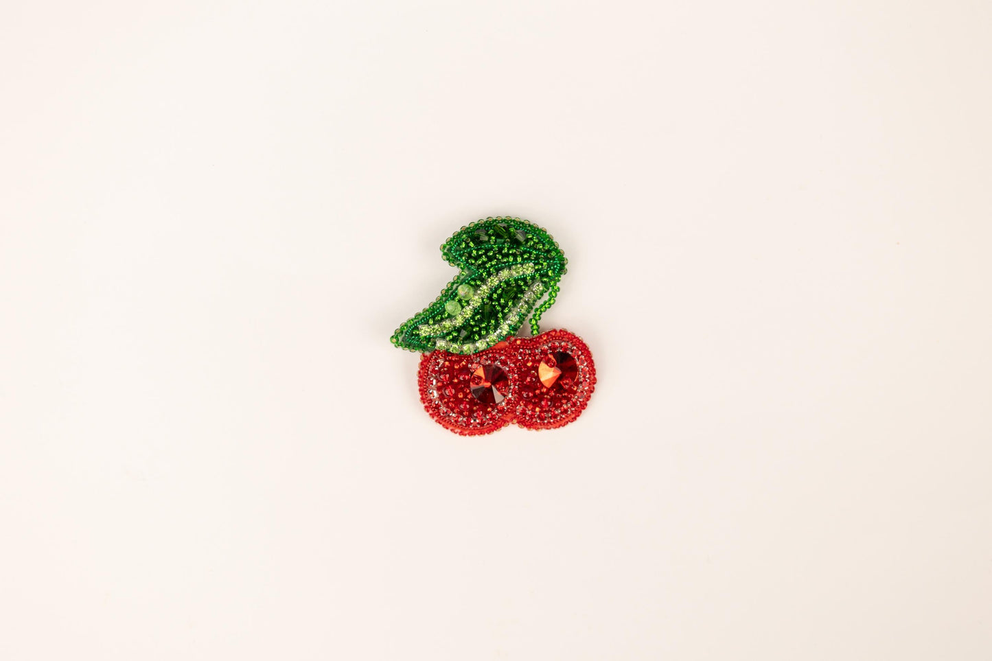 a brooch with a green leaf and two red cherries