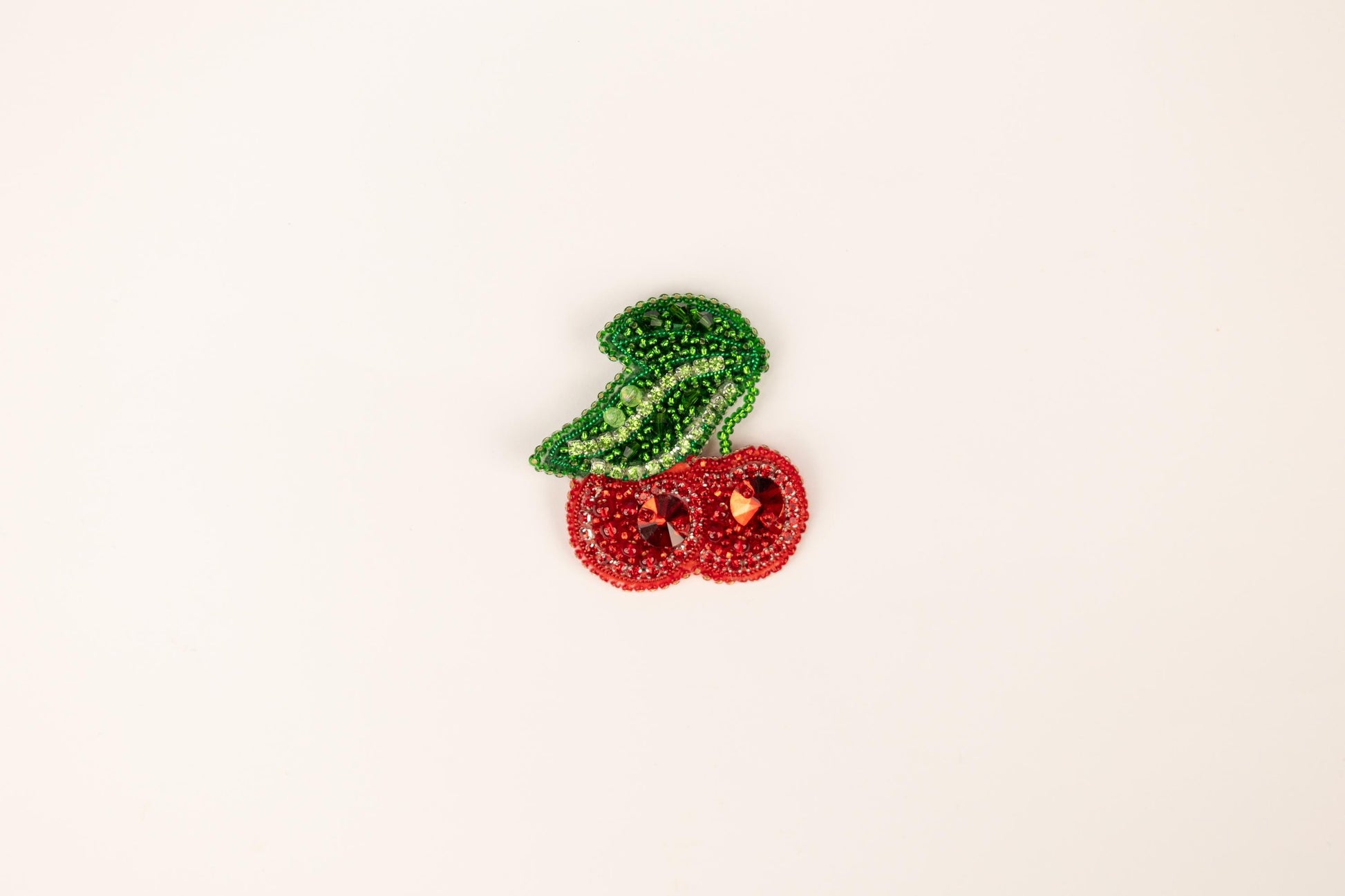 a brooch with a green leaf and two red cherries