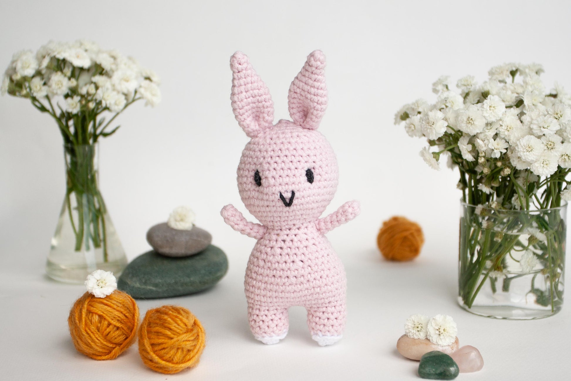 a crocheted bunny next to a vase of flowers and balls of yarn