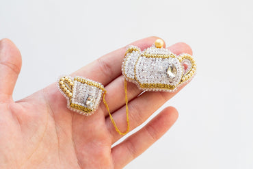 a hand holding two small white and gold jewelry pieces