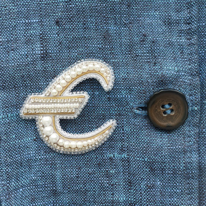 a close-up view of a blue fabric with a decorative letter 'E' made of pearls and rhinestones, and a button on the right side of the fabric.