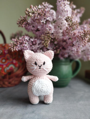 a crocheted cat sitting next to a vase of flowers