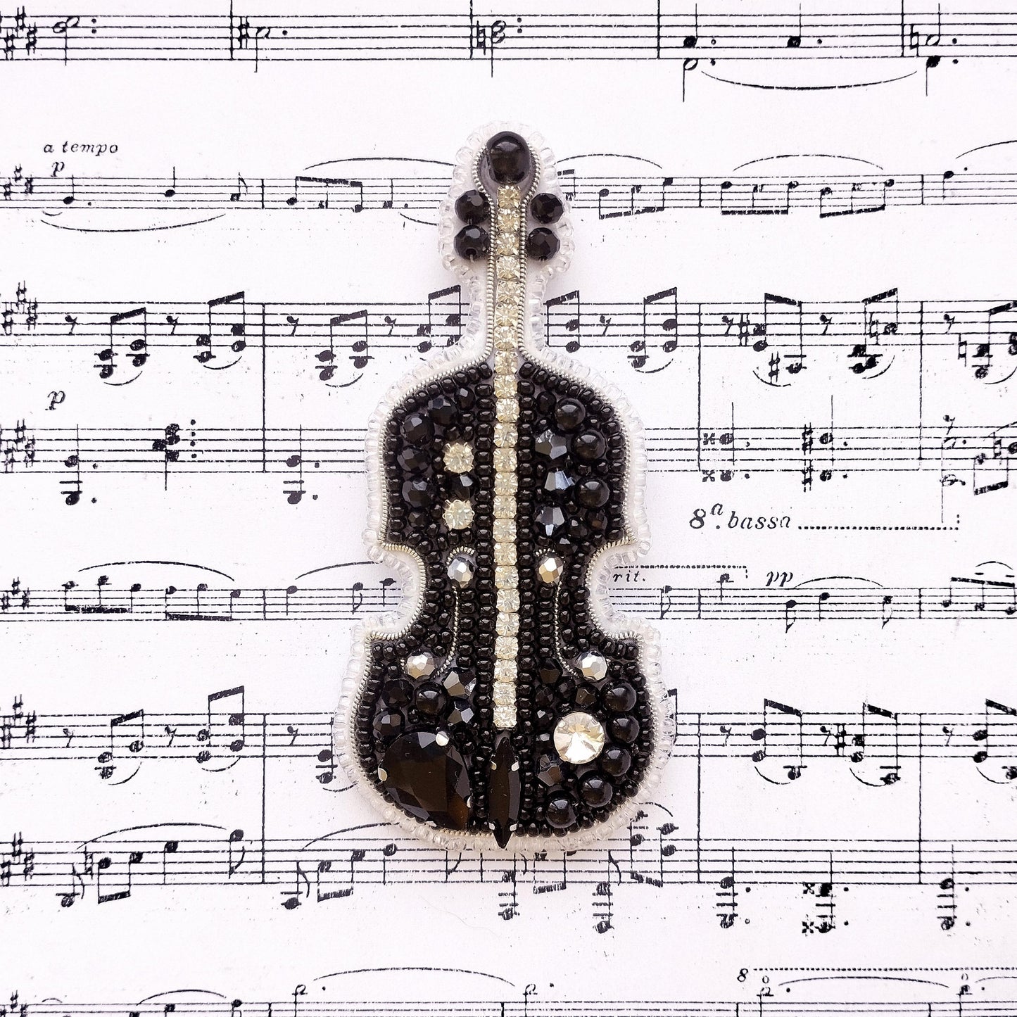 A black and silver violin brooch is displayed on top of sheet music.