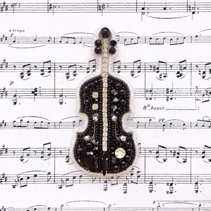 A black and silver violin brooch is displayed on top of sheet music.