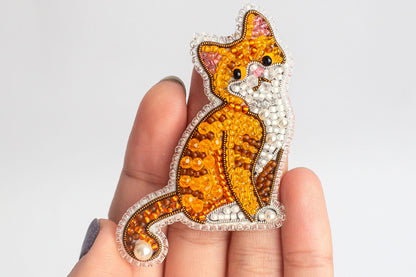 A hand holding a decorative beaded cat pin.
