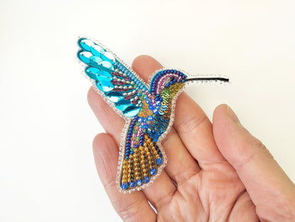a hand holding a beaded bird ornament