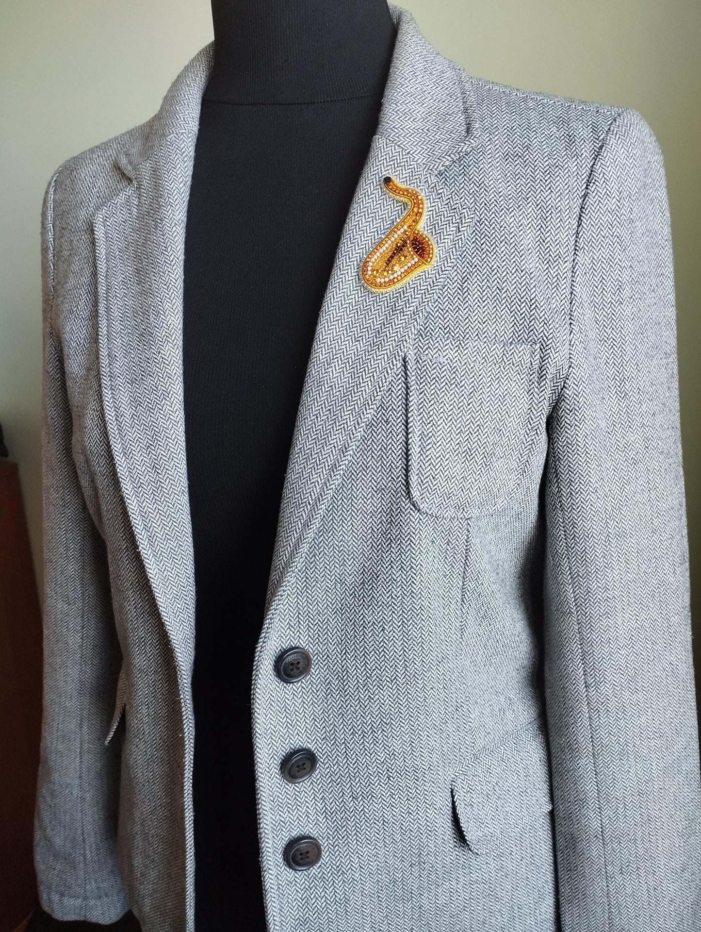 A gray tweed jacket with a black turtleneck and a decorative orange snake pin on the lapel.