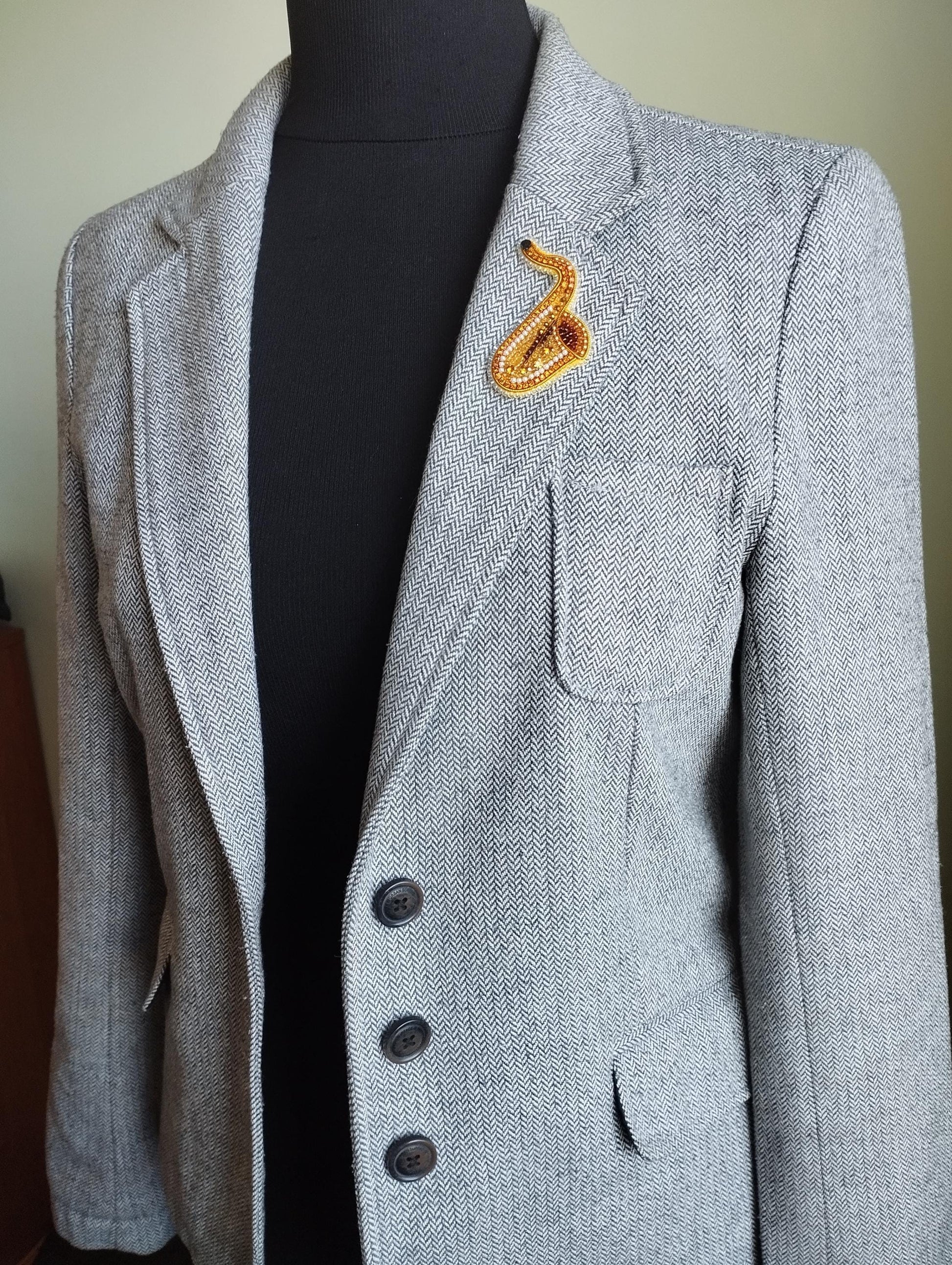 A gray tweed jacket with a black turtleneck and a decorative orange snake pin on the lapel.