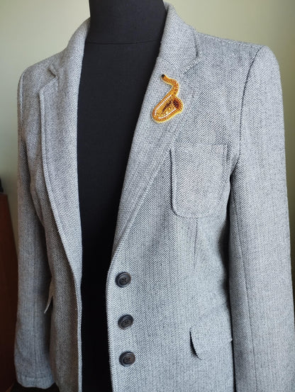 A gray tweed jacket with a black turtleneck and a decorative orange snake pin on the lapel.