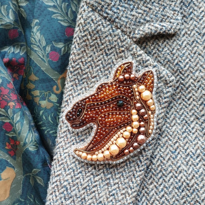 a close-up of a decorative beaded piece, possibly a brooch or pin, placed on a fabric with a floral pattern.