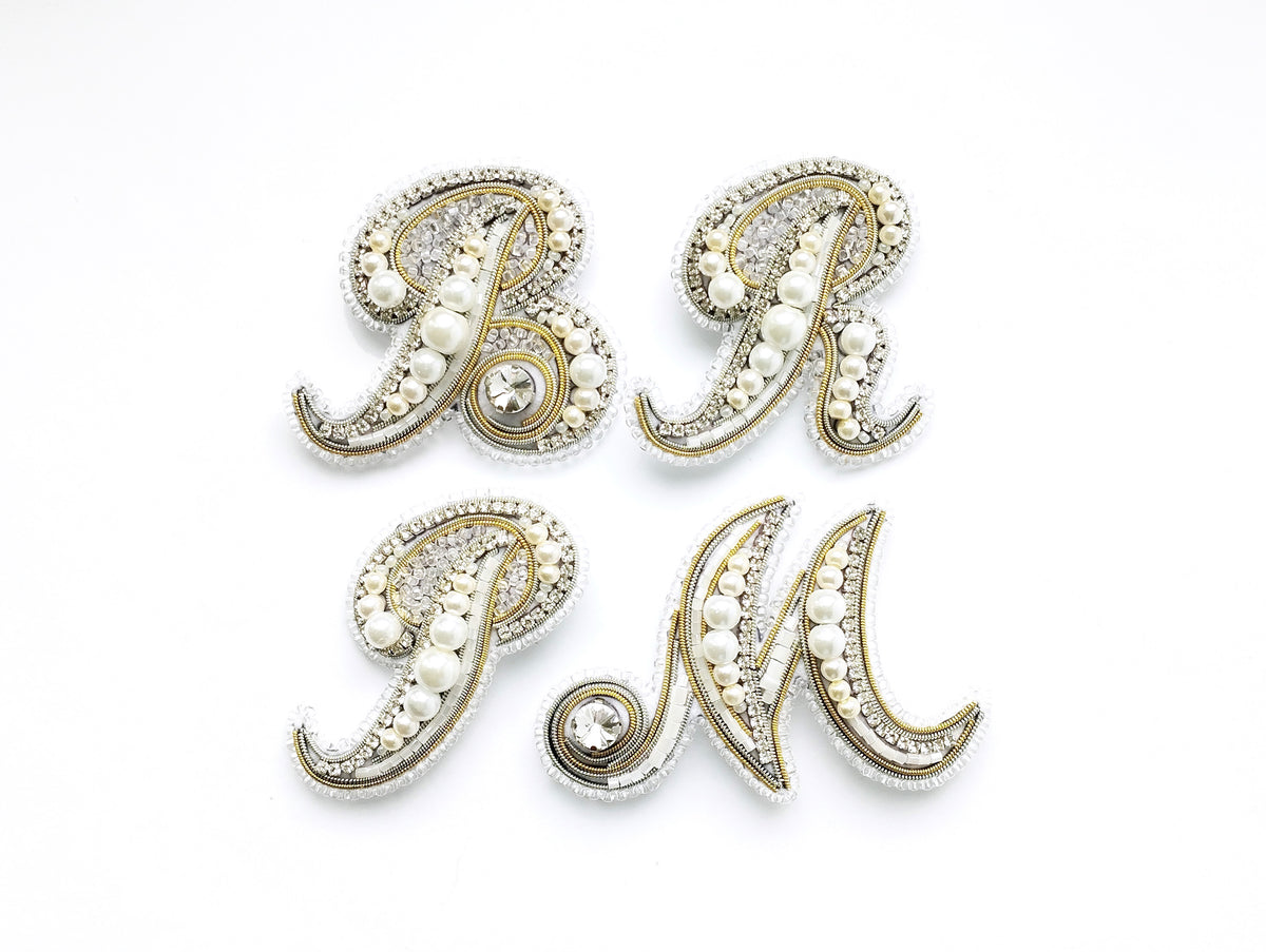 four decorative letters, each adorned with pearls and rhinestones, arranged in a square formation.