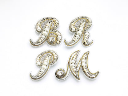 four decorative letters, each adorned with pearls and rhinestones, arranged in a square formation.