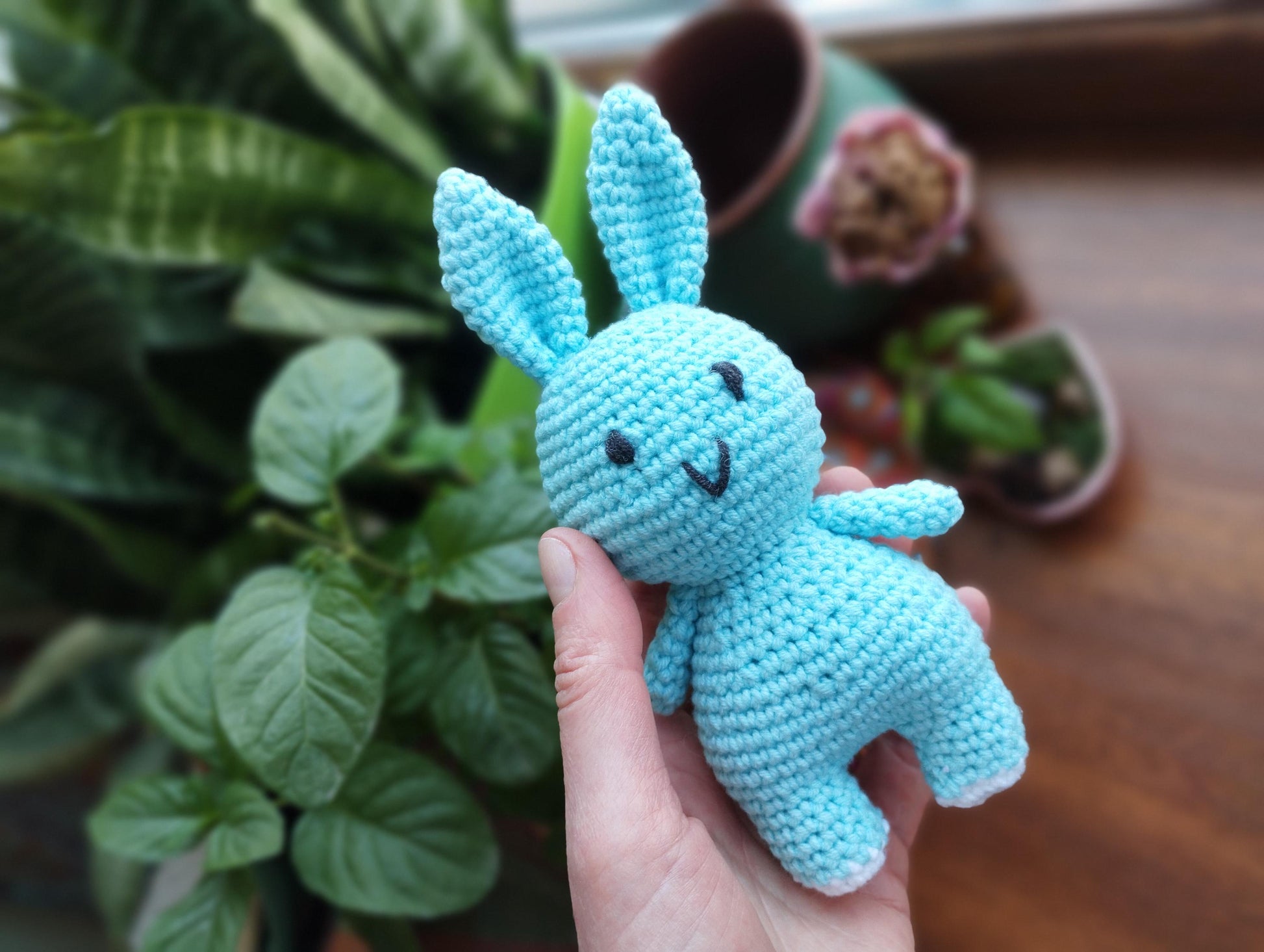 a hand holding a small blue crocheted bunny