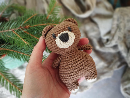 a hand holding a small brown teddy bear