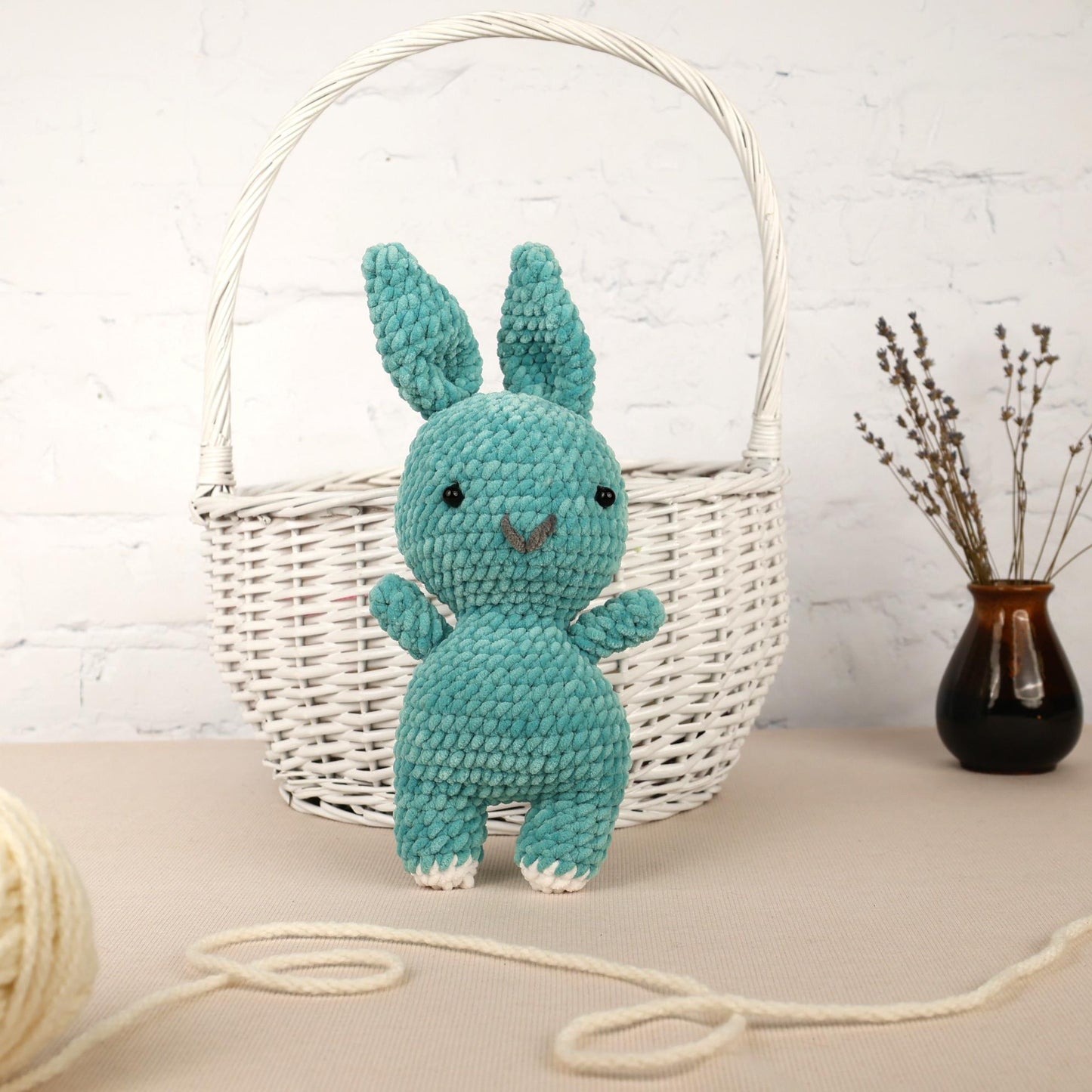 a crocheted blue bunny sitting next to a white basket