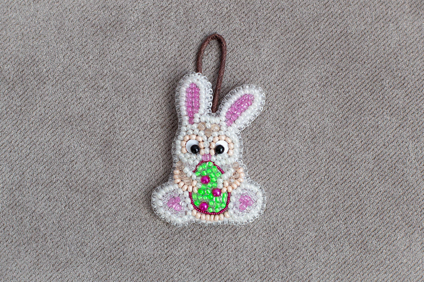 A beaded Easter bunny ornament is displayed on a grey textured surface.