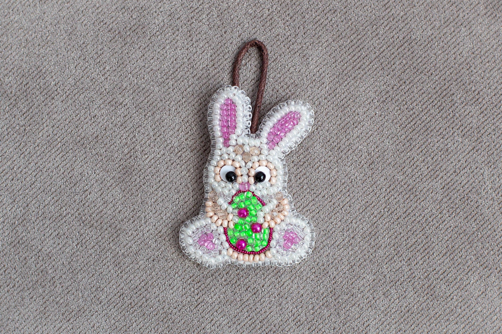 A beaded Easter bunny ornament is displayed on a grey textured surface.
