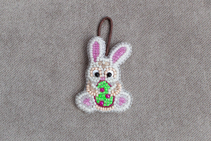 A beaded Easter bunny ornament is displayed on a grey textured surface.