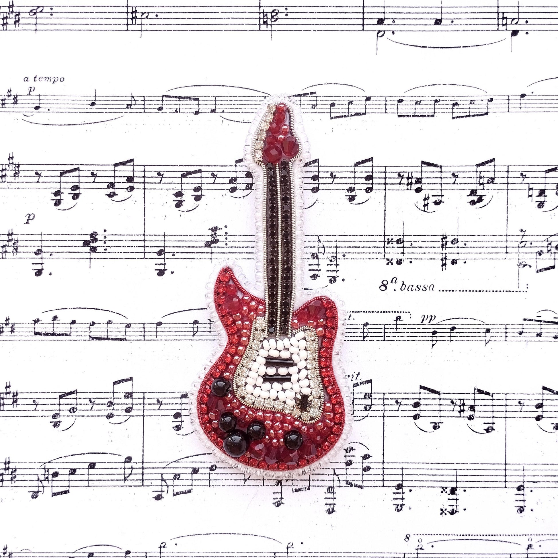 A red and white guitar-shaped embellishment is placed on top of sheet music with musical notes surrounding it.