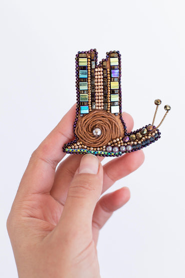 a hand holding a beaded brooch with a design on it