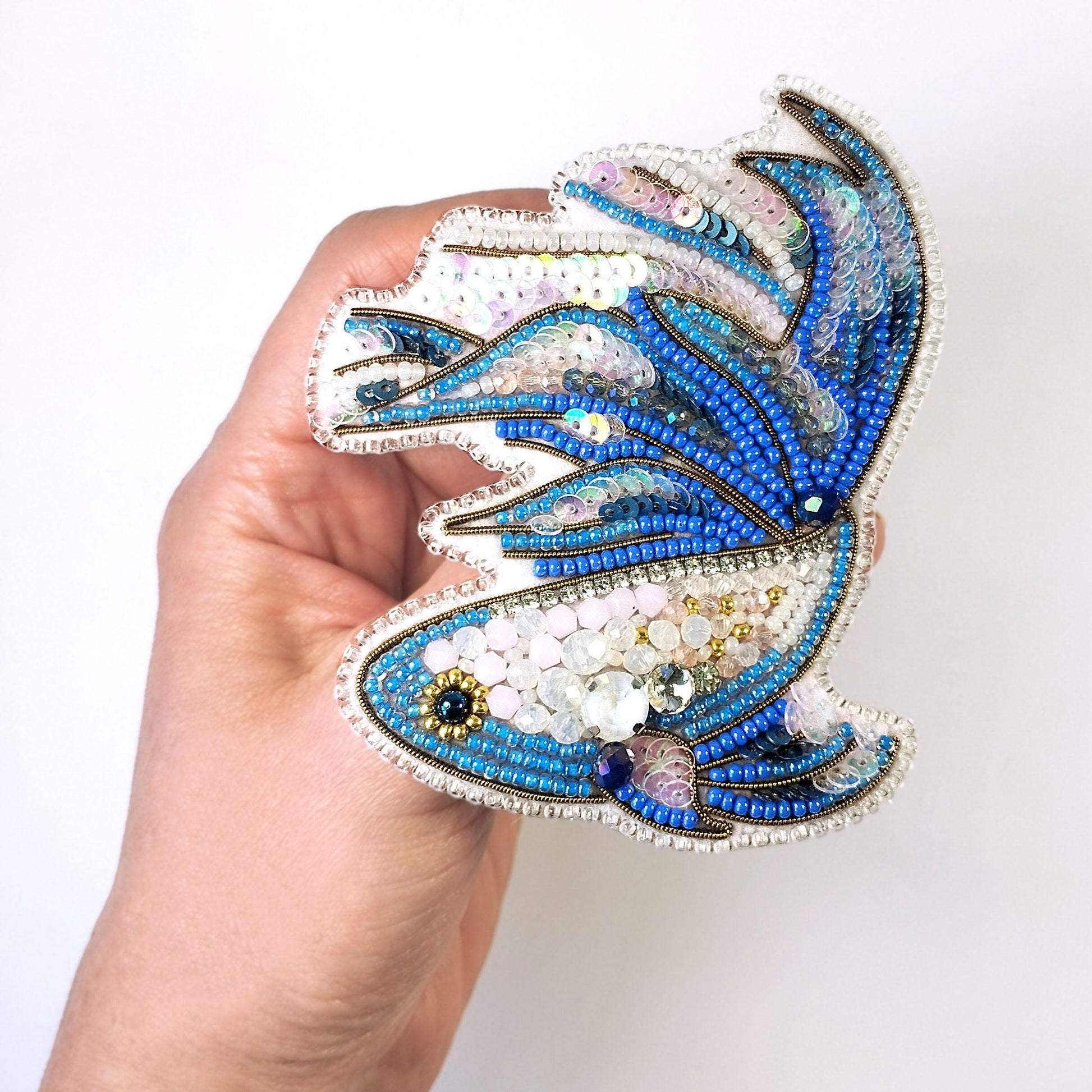 A hand holding a decorative beaded object resembling a fish or sea creature.