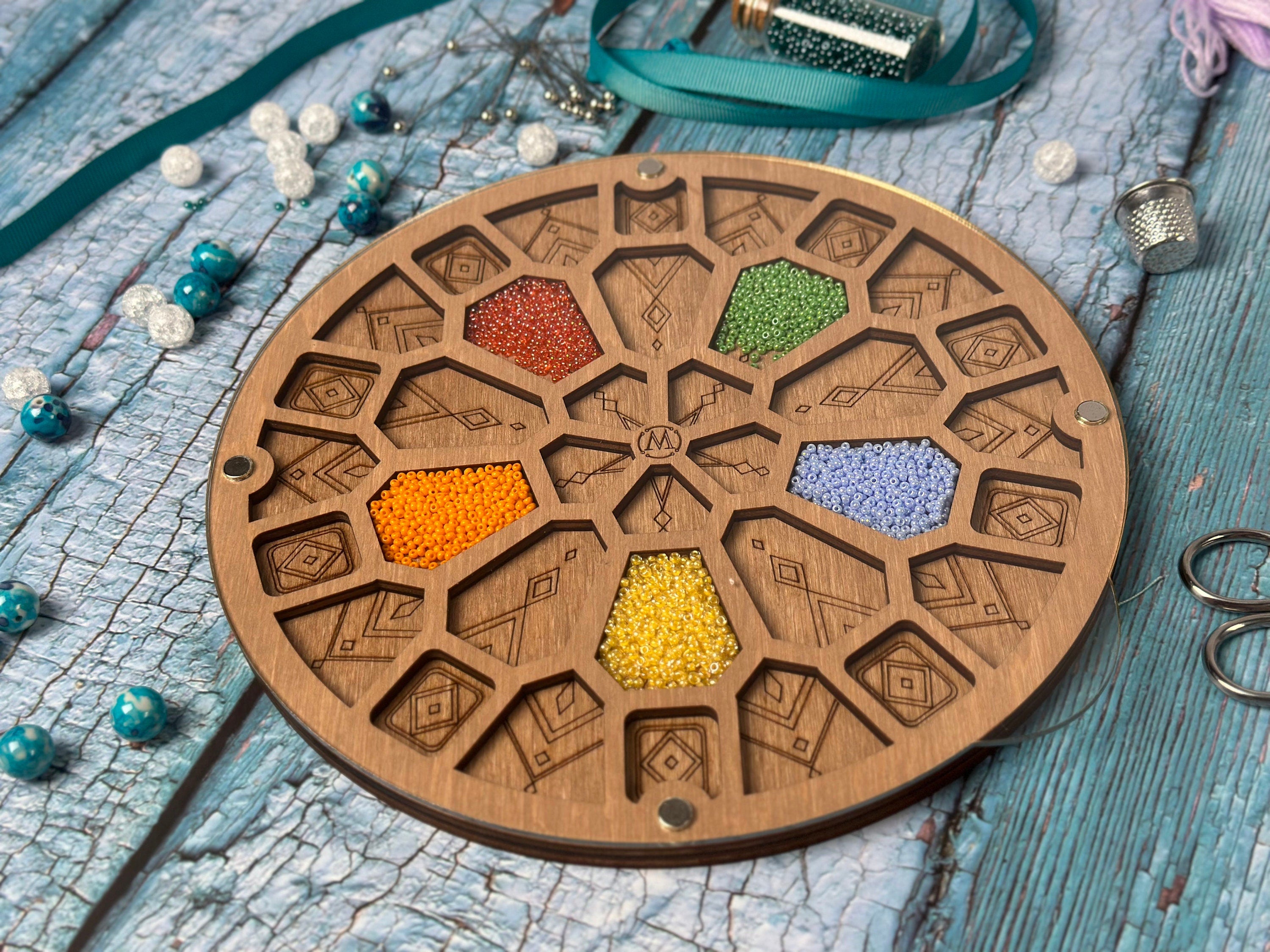 a round wooden tray with beads and a pair of scissors next to it