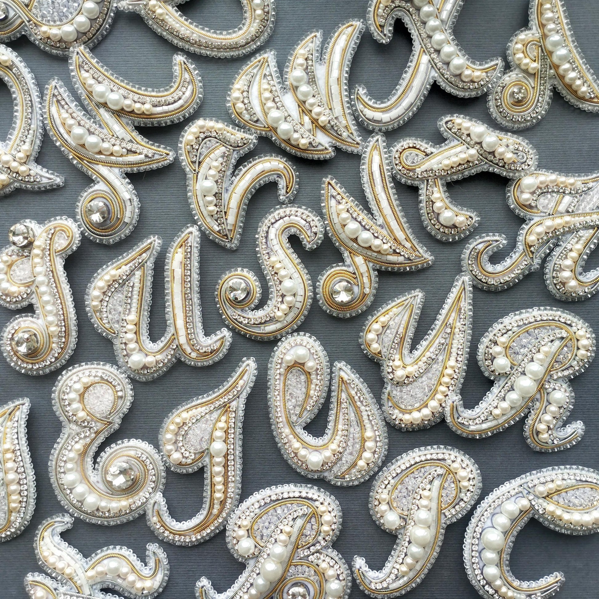 a collection of ornate, bejeweled letter shapes arranged in a grid-like pattern against a dark background.