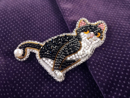 A decorative cat brooch made of beads and pearls, featuring a black and white color scheme with a detailed design.