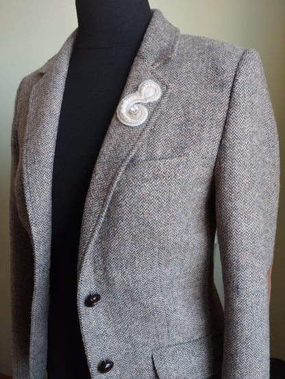 A gray tweed blazer with a white brooch on the left side of the chest.