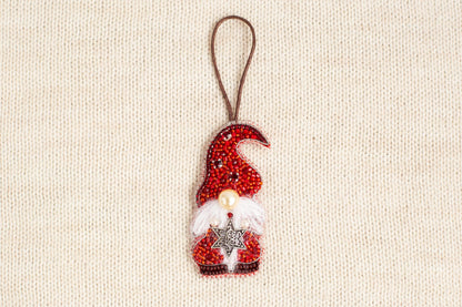 A red ornament resembling a gnome or dwarf figure, adorned with a star and pearls, is displayed against a beige background.