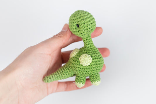 a hand holding a small green crocheted toy