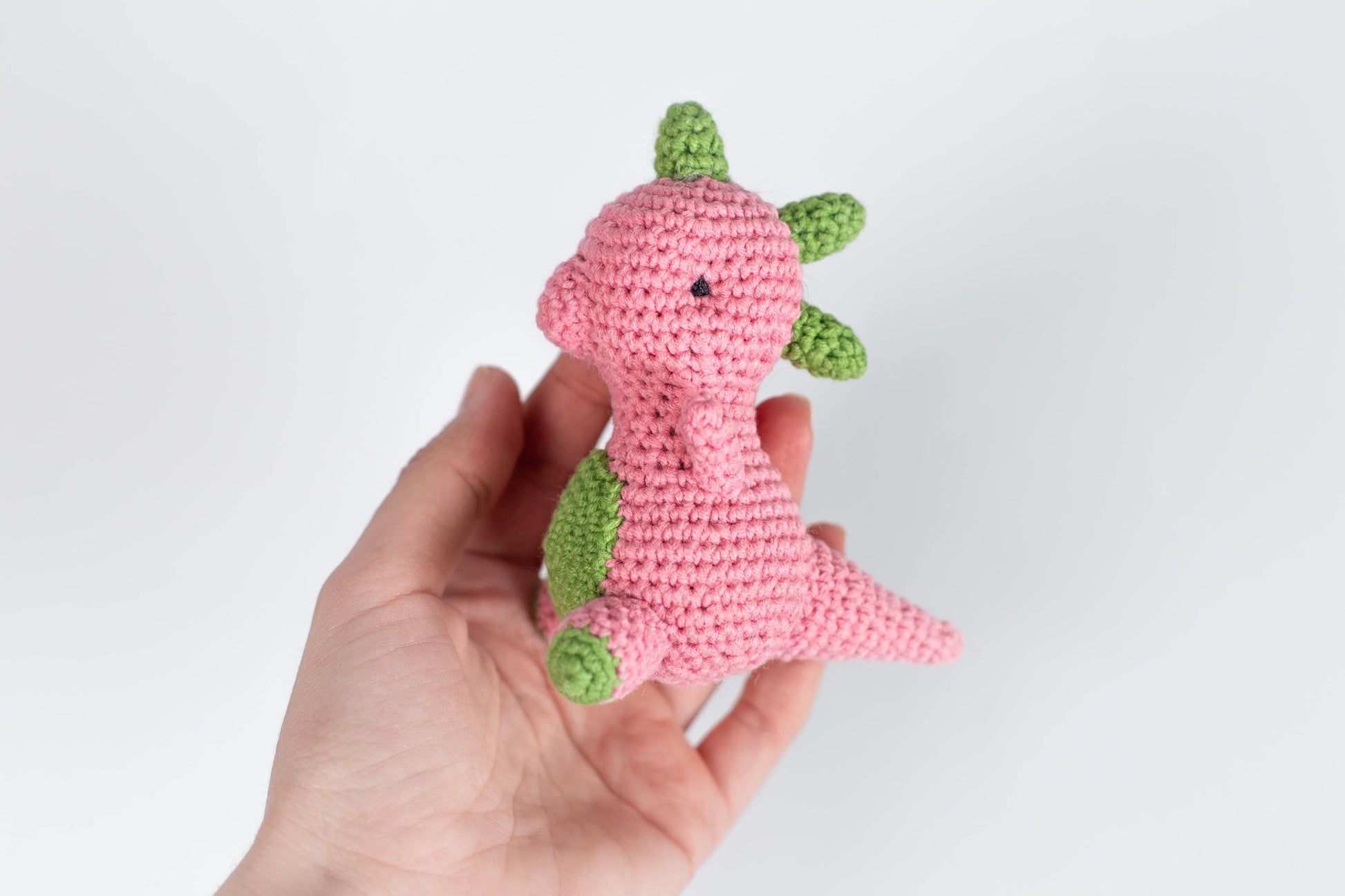 a hand holding a pink crocheted stuffed animal