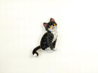 A decorative cat brooch made of beads and pearls, featuring a black and white color scheme.
