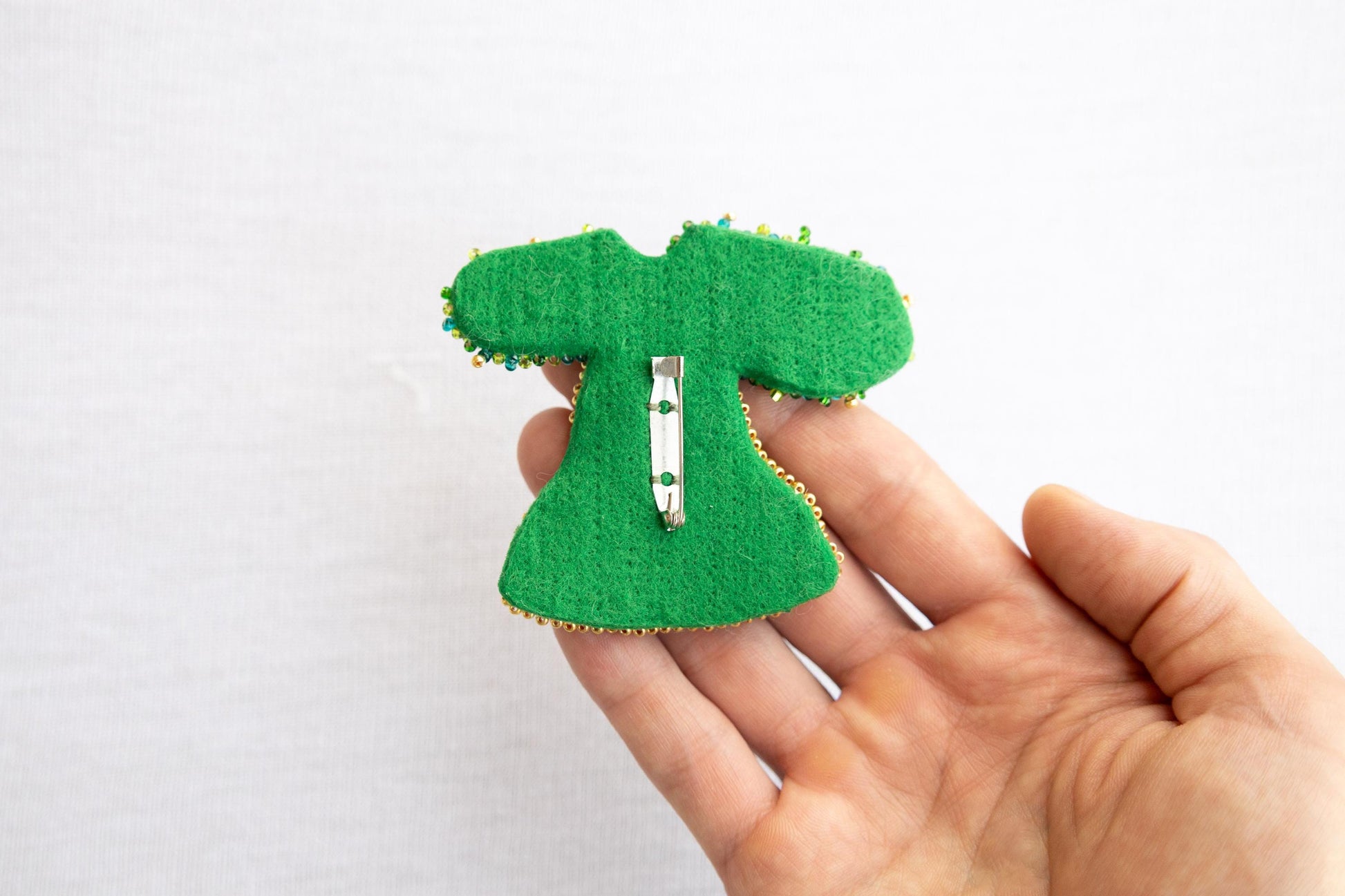 a person is holding a green brooch with a green dress on it