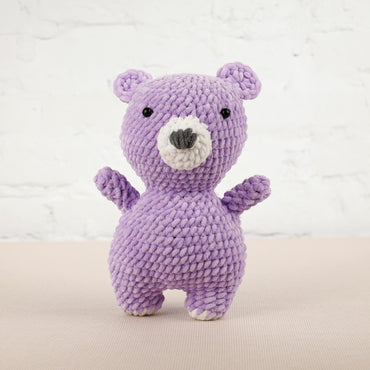 a purple knitted teddy bear standing on its hind legs