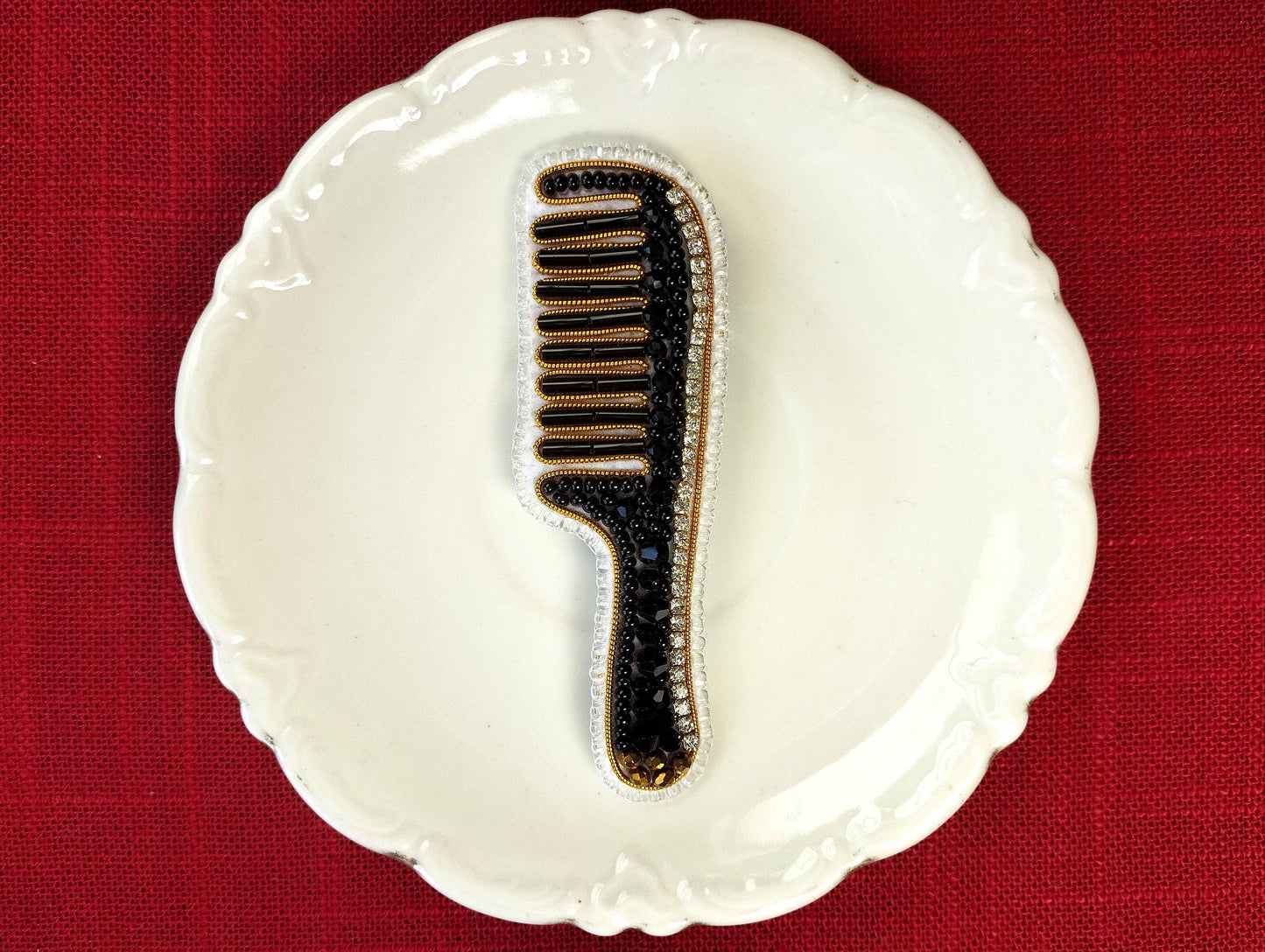 A white ceramic plate with a black and gold comb-like object placed on it, set against a red background.