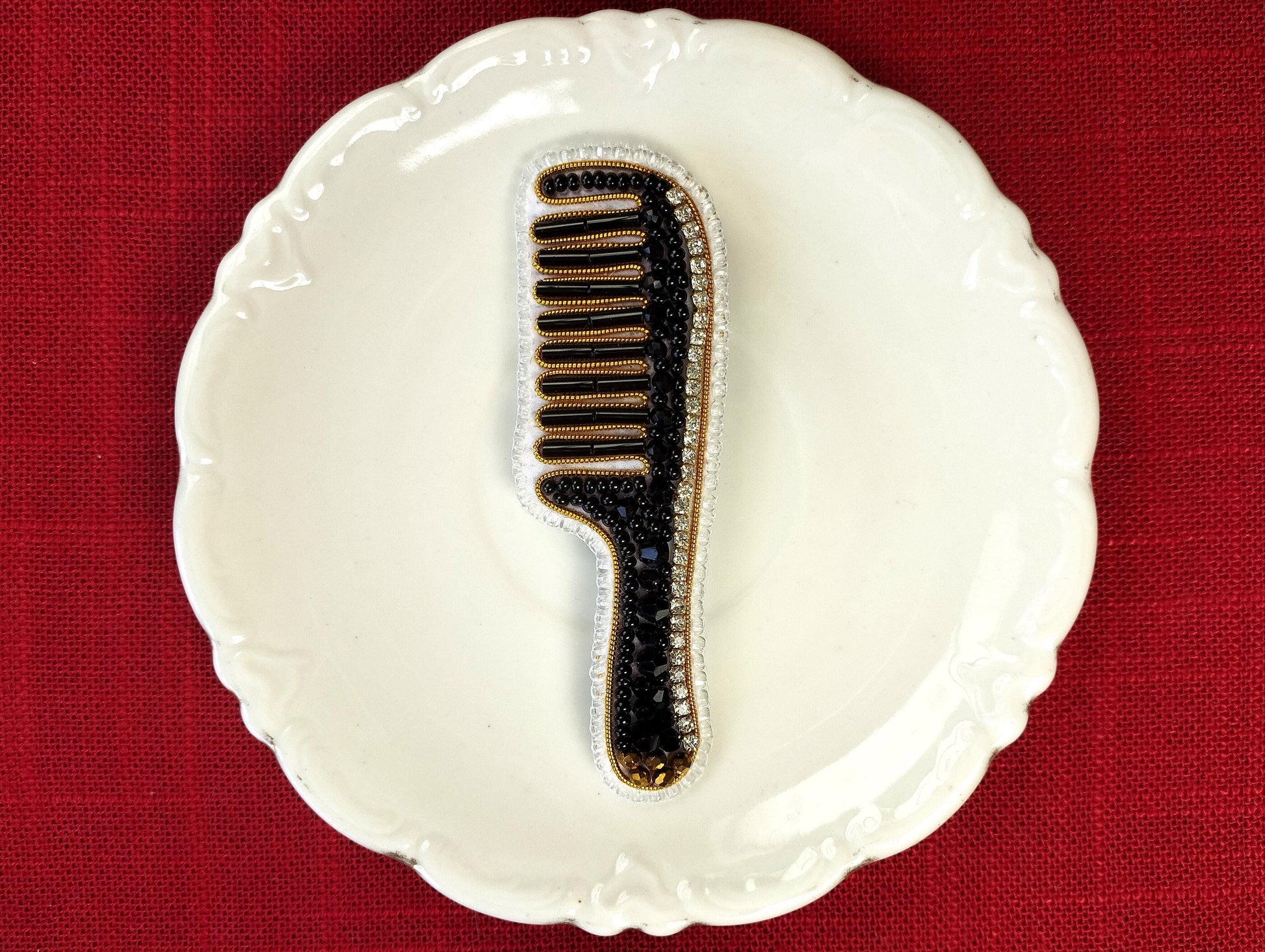 A white ceramic plate with a black and gold comb-like object placed on it, set against a red background.
