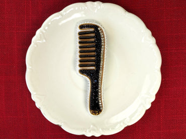 A white ceramic plate with a black and gold comb-like object placed on it, set against a red background.