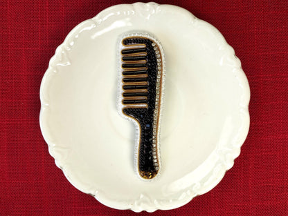 A white ceramic plate with a black and gold comb-like object placed on it, set against a red background.