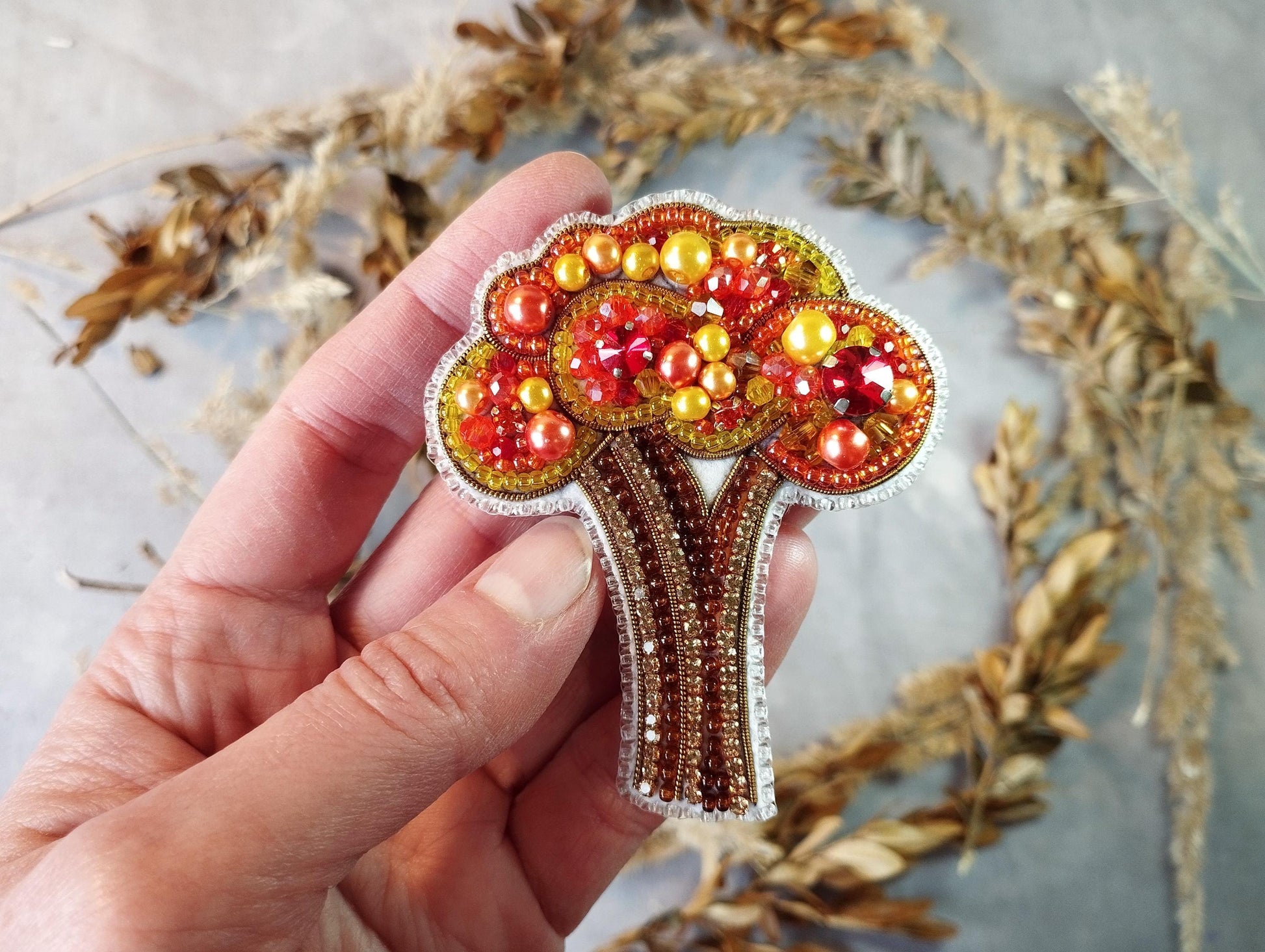 a hand holding a beaded brooch with a tree on it