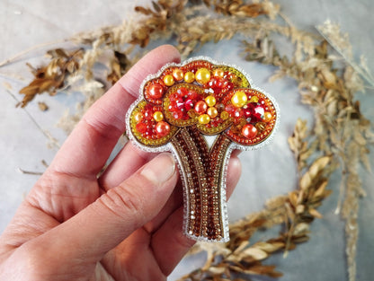 a hand holding a beaded brooch with a tree on it