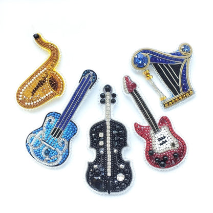 five colorful and intricately designed musical instruments, including a saxophone, a harp, a guitar, a violin, and a cello, all adorned with sparkling rhinestones or crystals.
