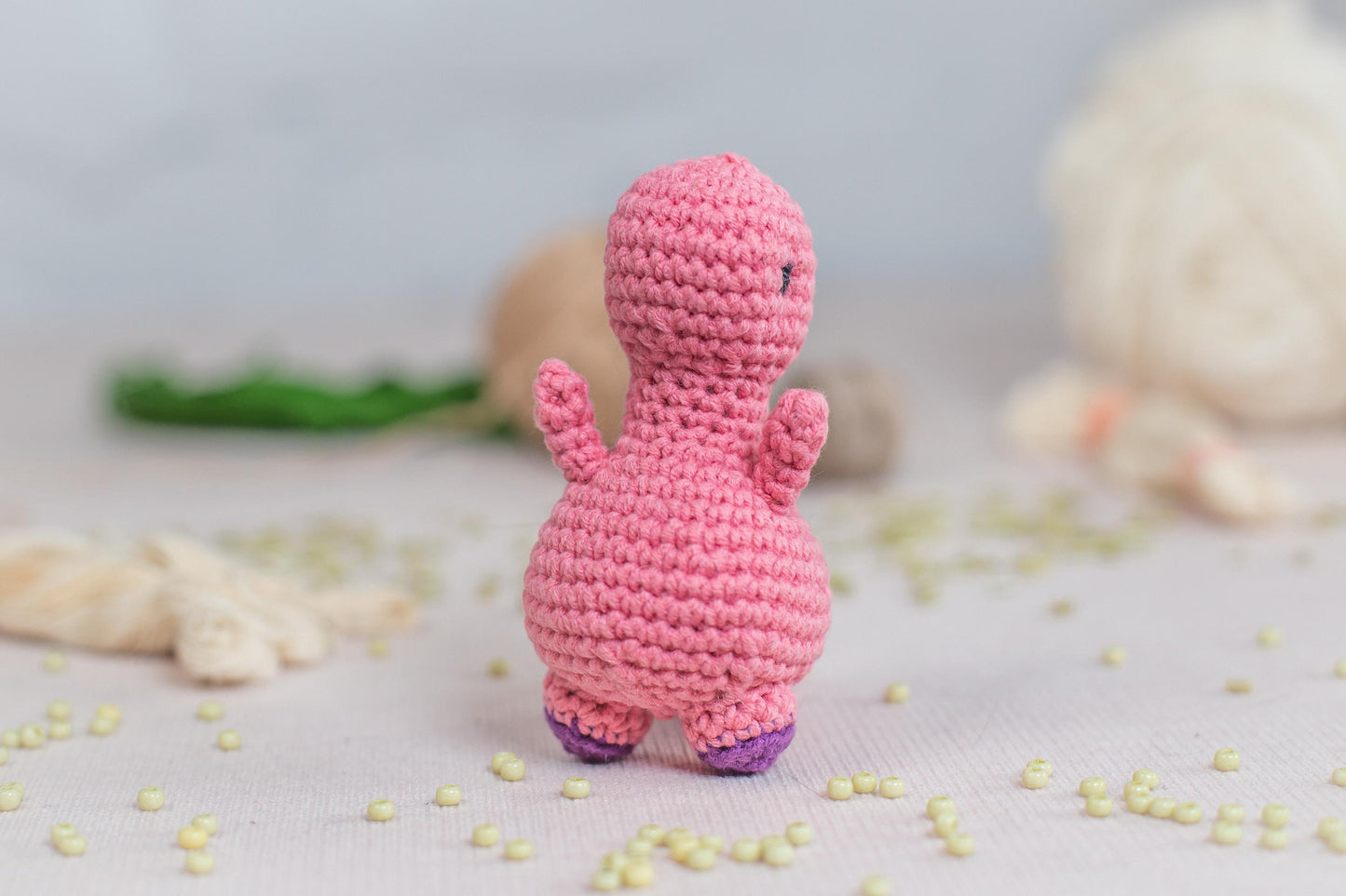 a pink crocheted toy standing next to a ball of yarn