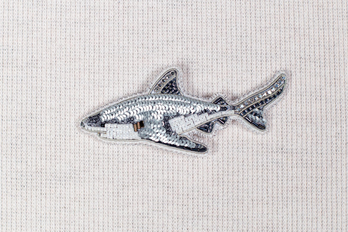 a silver sequin shark embroidered on a fabric surface.
