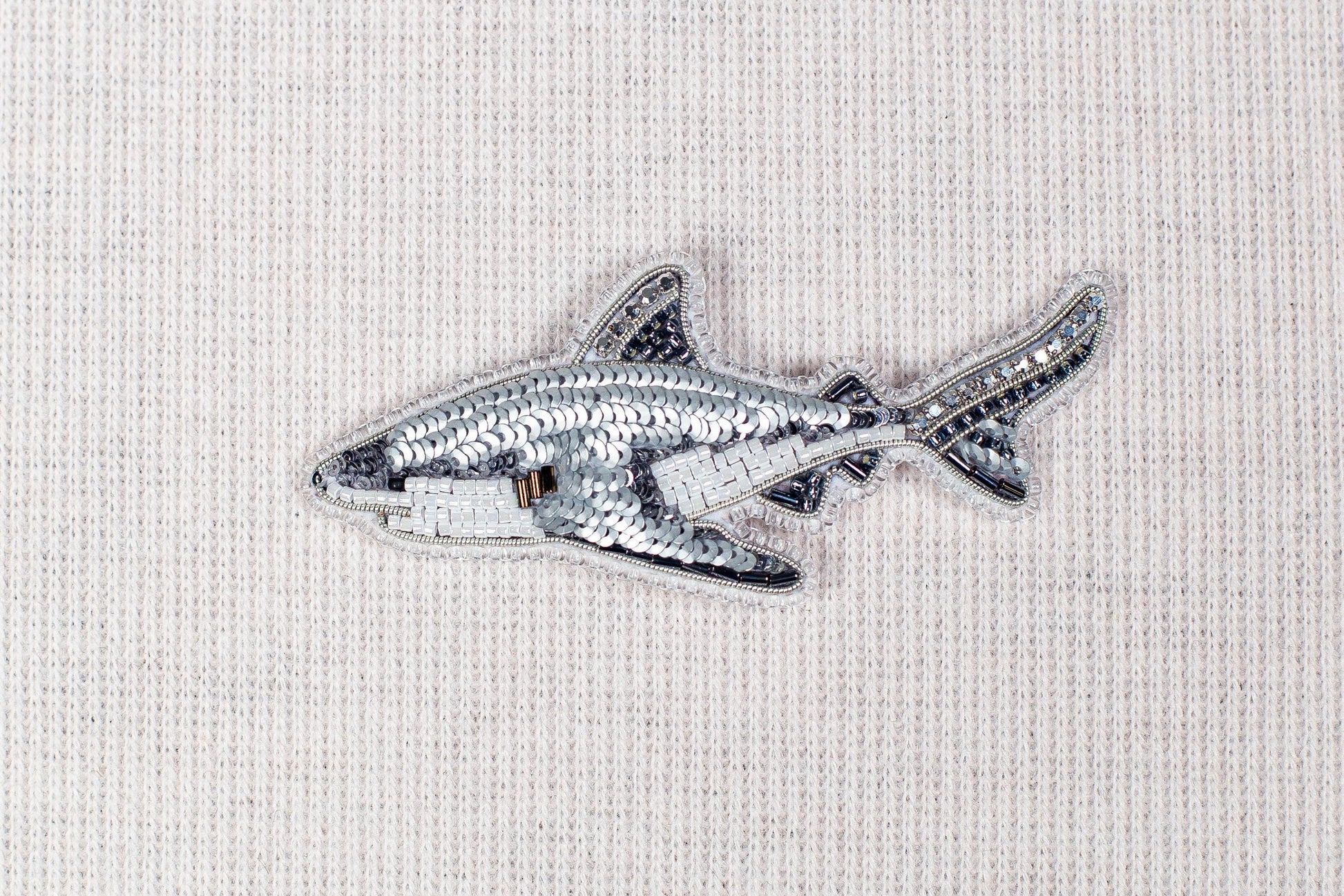 a silver sequin shark embroidered on a fabric surface.