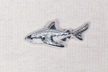 a silver sequin shark embroidered on a fabric surface.