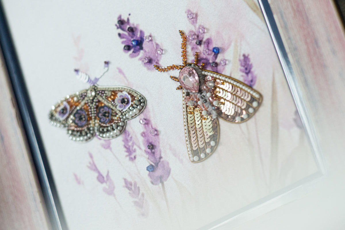 two butterflies, one with a metallic appearance and the other with a floral design, set against a background of purple flowers.