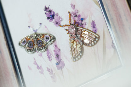 two butterflies, one with a metallic appearance and the other with a floral design, set against a background of purple flowers.